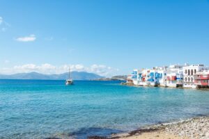 A stunning view of Mykonos with iconic white buildings and a sailboat on the turquoise water.