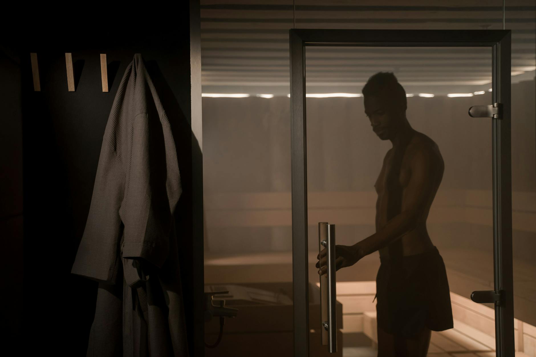 A silhouette of a man entering a sauna through a glass door, capturing a serene spa atmosphere.