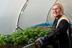 An elderly woman tending to plants in a greenhouse, showcasing horticulture in Greater Manchester.