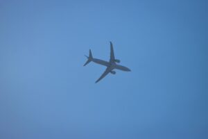Silhouette of an airplane in flight over Corfu, Greece, with a clear blue sky background.