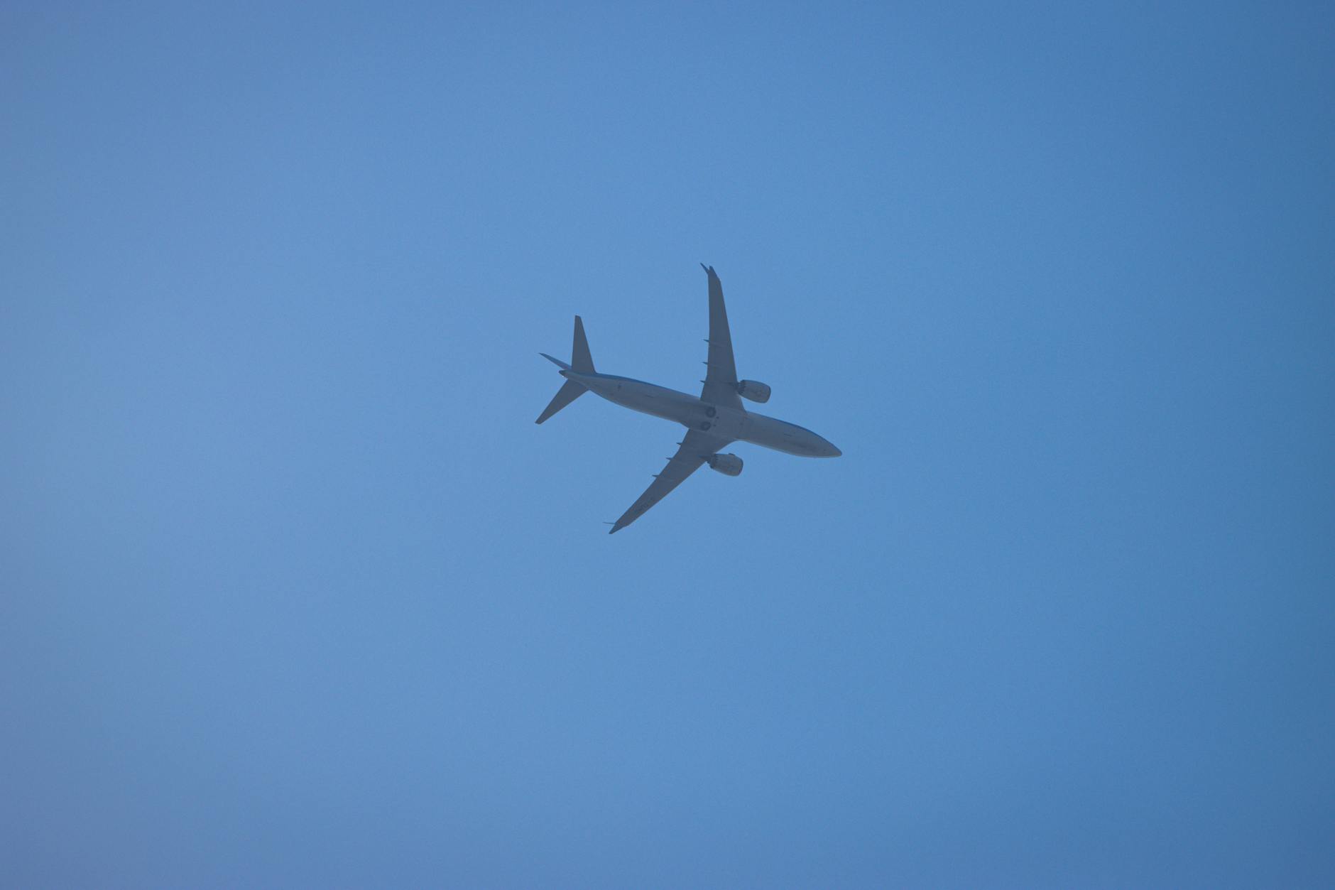 Silhouette of an airplane in flight over Corfu, Greece, with a clear blue sky background.
