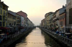 View of Naviglio Grande canal at sunset in Milan, Italy, flanked by colorful buildings and bustling streets.