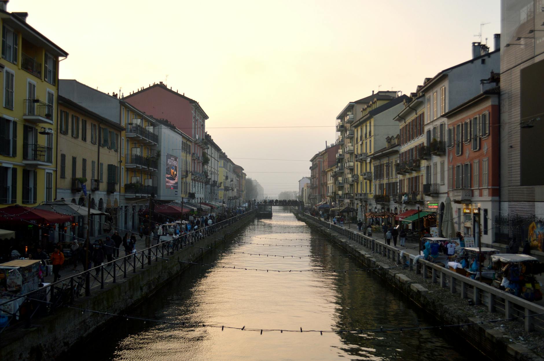 View of Naviglio Grande canal at sunset in Milan, Italy, flanked by colorful buildings and bustling streets.